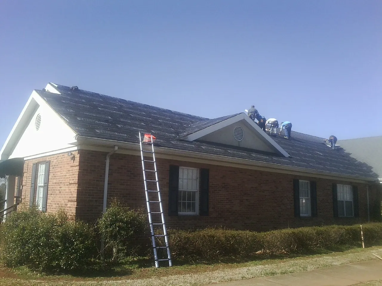 Crew tearing shingles off a brick ranch roof with a ladder set — Metal Roof Repair work by our crew in South Grafton