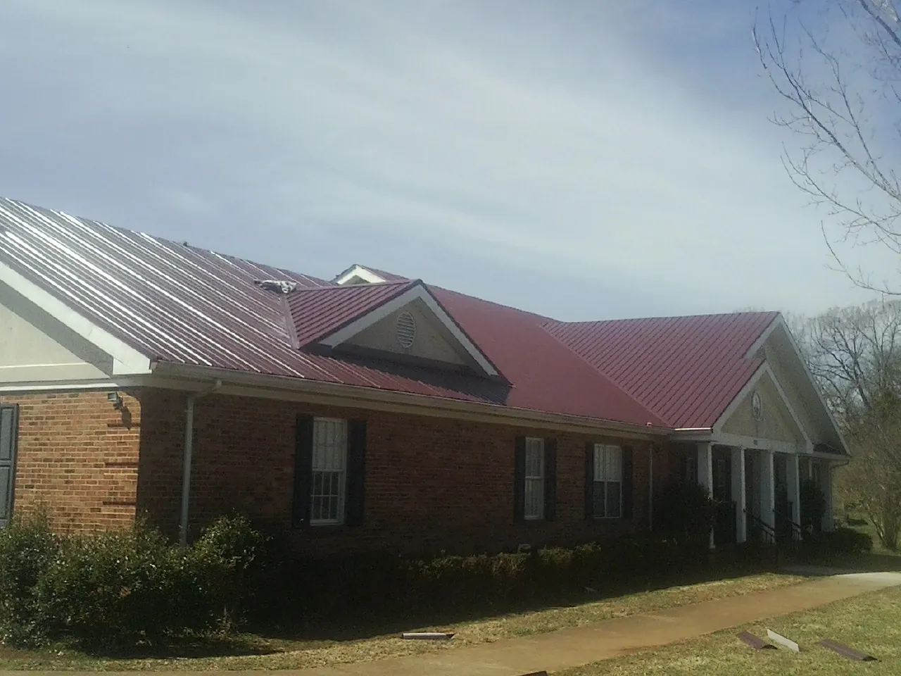 Red metal roof with gabled entries on a long brick building, from a Hail Damage Roof Repair job in South Grafton