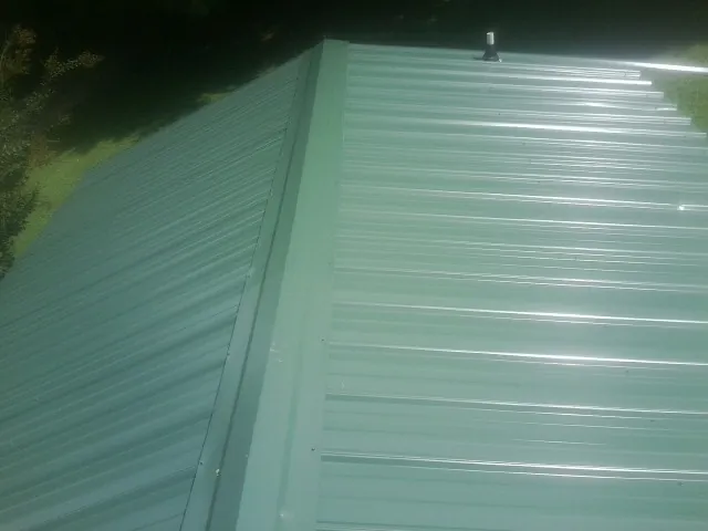 New green metal panels meeting at the ridge of a roof — Flat Roof Repair work by our crew in South Grafton
