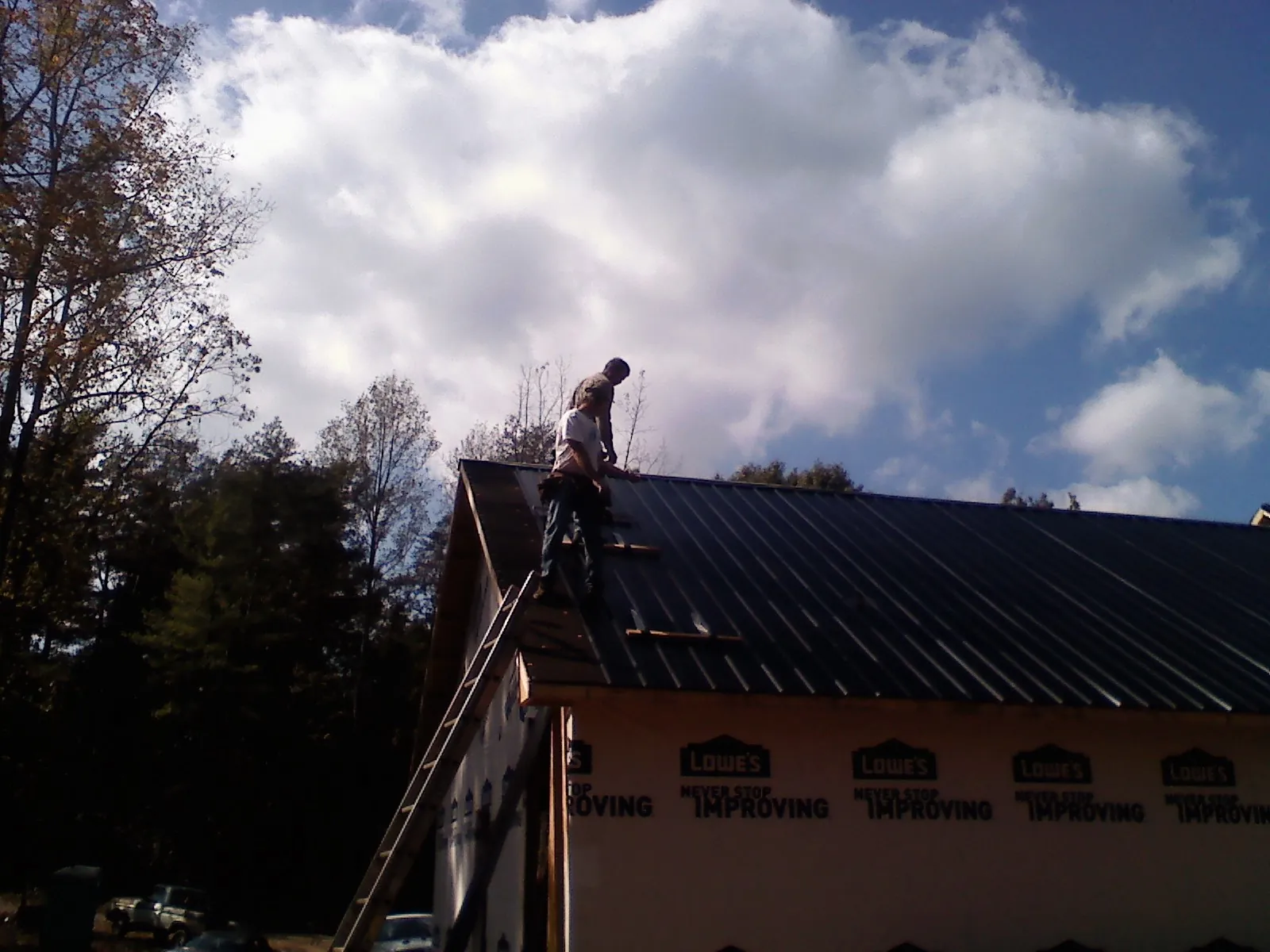Roofer fastening dark metal panels high against a cloudy sky, from a Roof Inspection job in South Grafton
