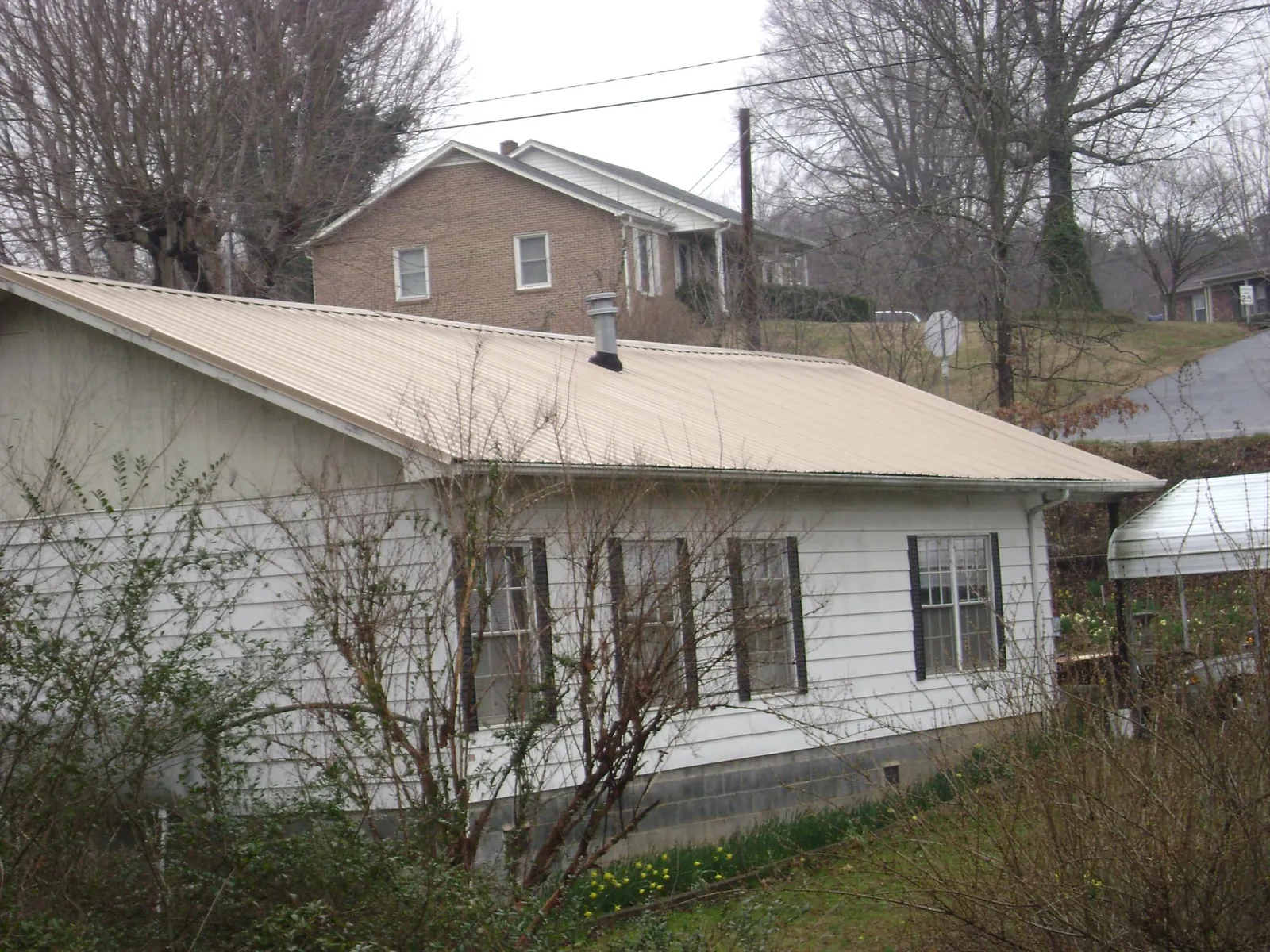 Tan metal roof on a white sided house set into a hillside — Commercial Roofing by Roofing Brothers in South Grafton